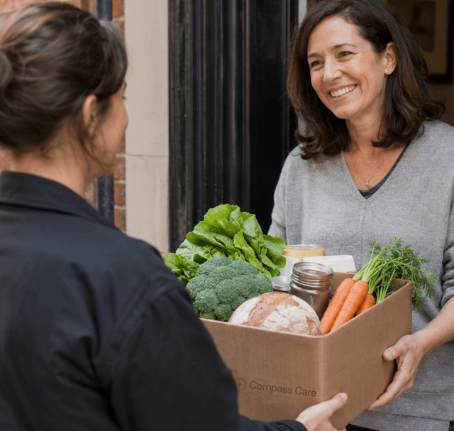 Delivery driver handing box of groceries to a woman at her doorstep